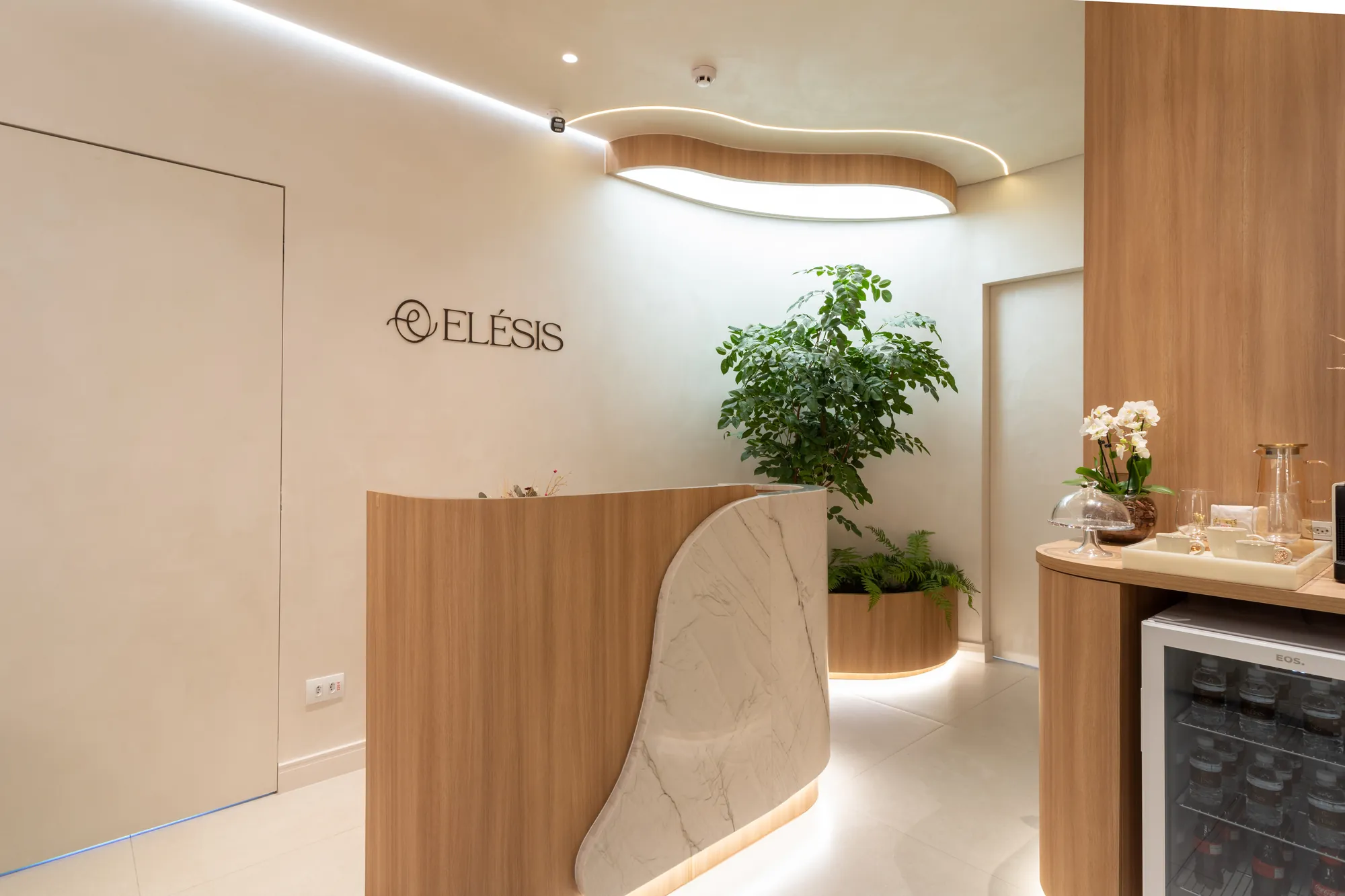 Recepção da clínica Elésis em Piracicaba, com marcenaria em madeira clara, bancada de mármore e o logotipo Elésis na parede